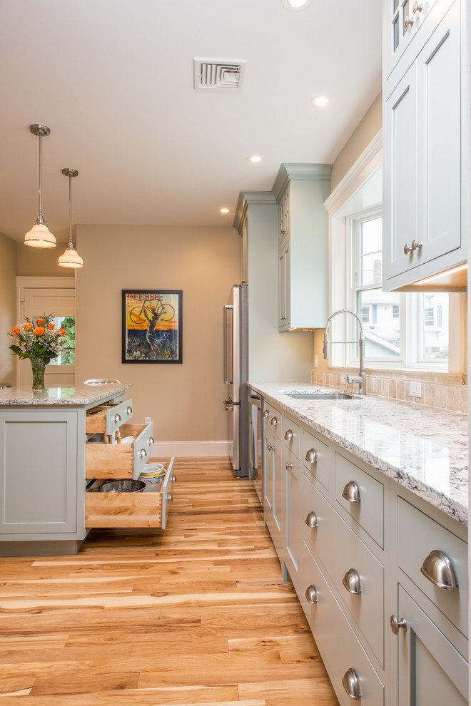 Mid-sized transitional l-shaped medium tone wood floor enclosed kitchen photo in Boston with an undermount sink, quartz countertops, beige backsplash, stone tile backsplash, stainless steel appliances, an island and shaker cabinets