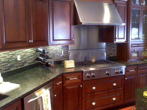 Inspiration for a large transitional medium tone wood floor kitchen remodel with an undermount sink, raised-panel cabinets, dark wood cabinets, granite countertops, multicolored backsplash, matchstick tile backsplash, stainless steel appliances and an island