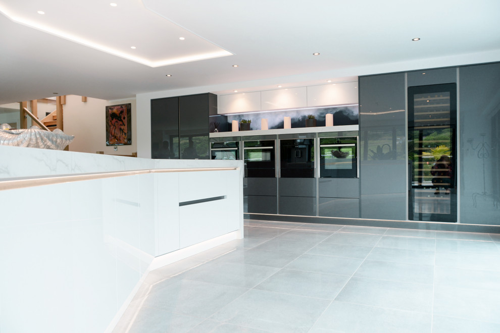 This is an example of an expansive modern open plan kitchen in Cornwall with flat-panel cabinets, grey cabinets, quartz benchtops, blue splashback, glass sheet splashback, with island and white benchtop.