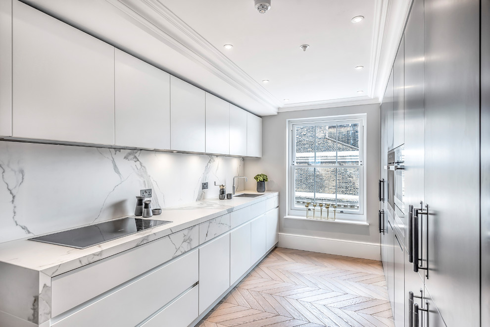 Contemporary galley kitchen in London with flat-panel cabinets, white cabinets, white splashback, stone slab splashback, medium hardwood floors, no island, brown floor and white benchtop.