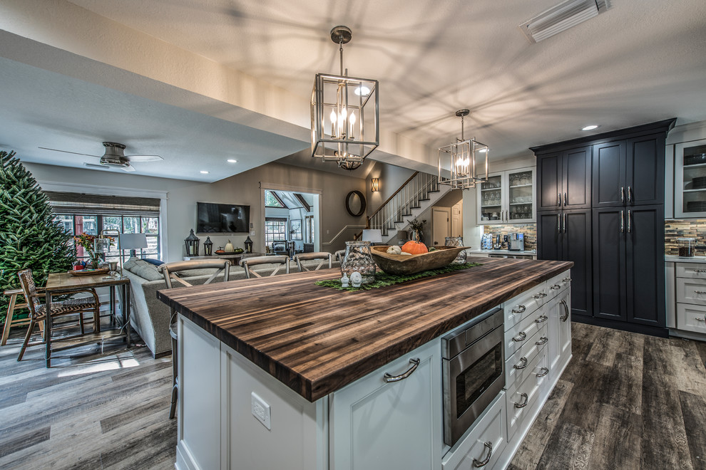 Large country u-shaped eat-in kitchen in Tampa with a farmhouse sink, recessed-panel cabinets, white cabinets, wood benchtops, white splashback, stone tile splashback, stainless steel appliances, vinyl floors, with island and brown floor.