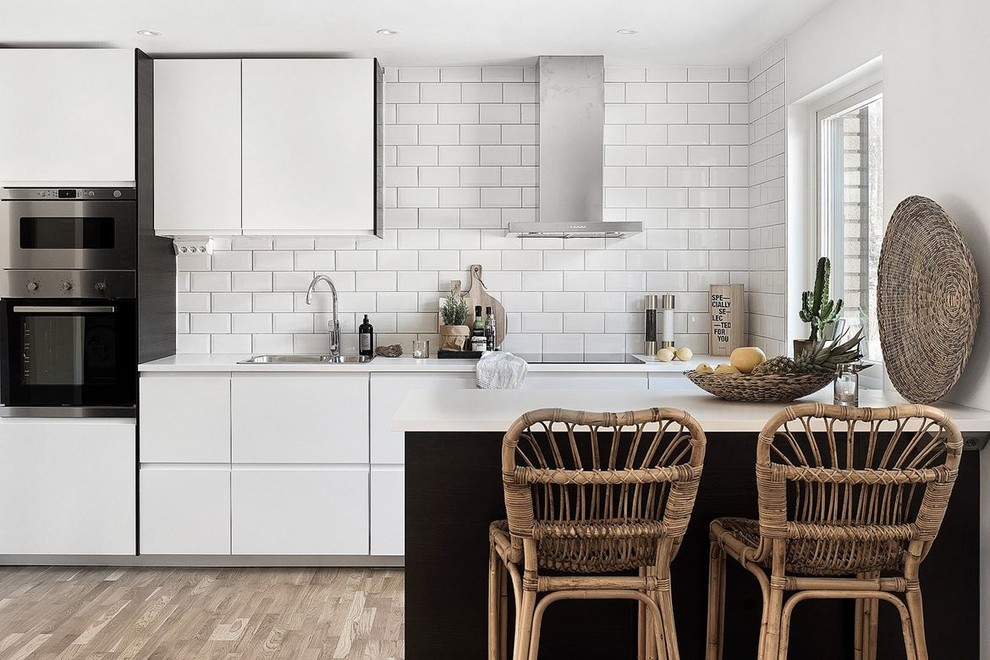 Scandinavian kitchen in Other with a drop-in sink, flat-panel cabinets, white cabinets, white splashback, subway tile splashback, light hardwood floors, a peninsula and beige floor.