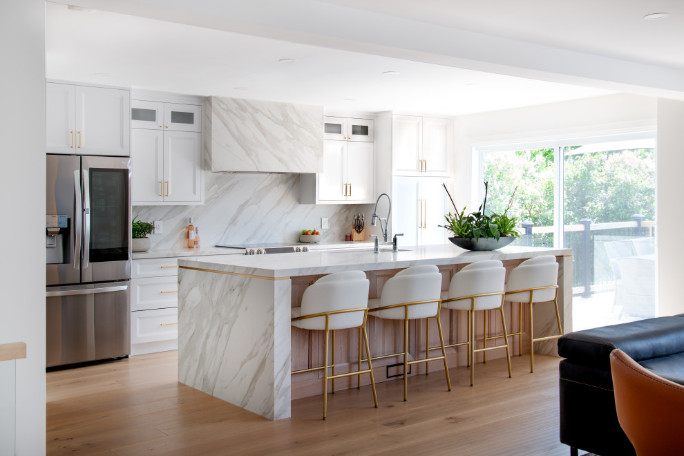 Mid-sized transitional galley light wood floor and beige floor open concept kitchen photo in Ottawa with an undermount sink, recessed-panel cabinets, white cabinets, quartz countertops, white backsplash, porcelain backsplash, stainless steel appliances, an island and white countertops