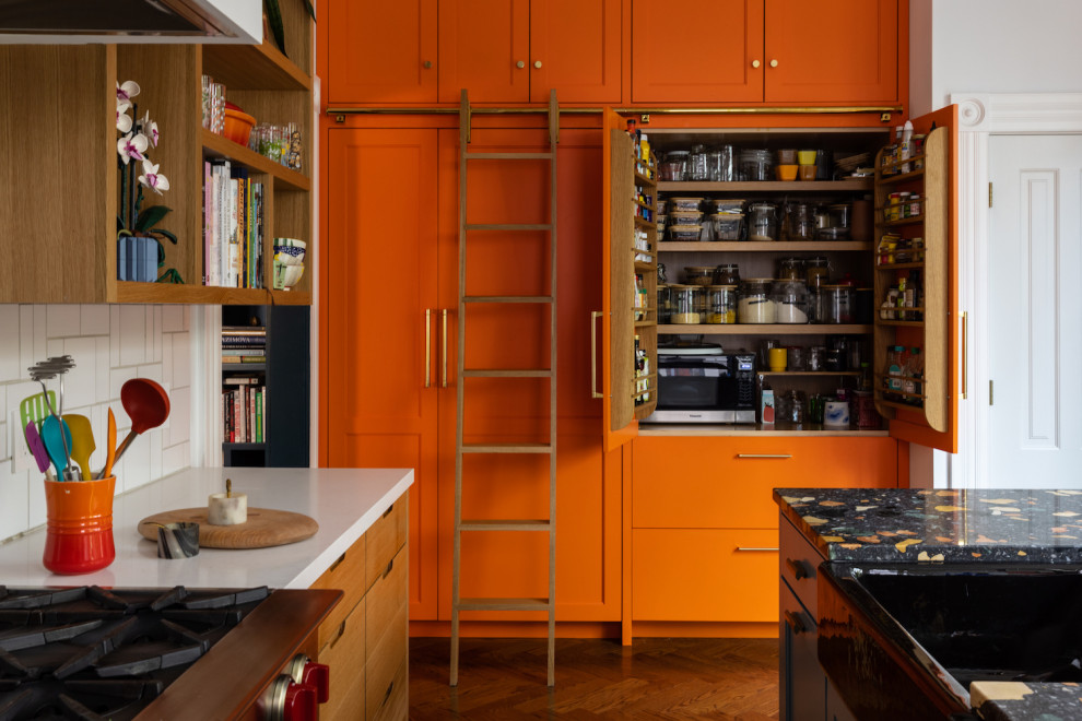 This is an example of an eclectic kitchen in San Francisco with a farmhouse sink, shaker cabinets, orange cabinets, quartz benchtops, white splashback, ceramic splashback, medium hardwood floors, with island and multi-coloured benchtop.