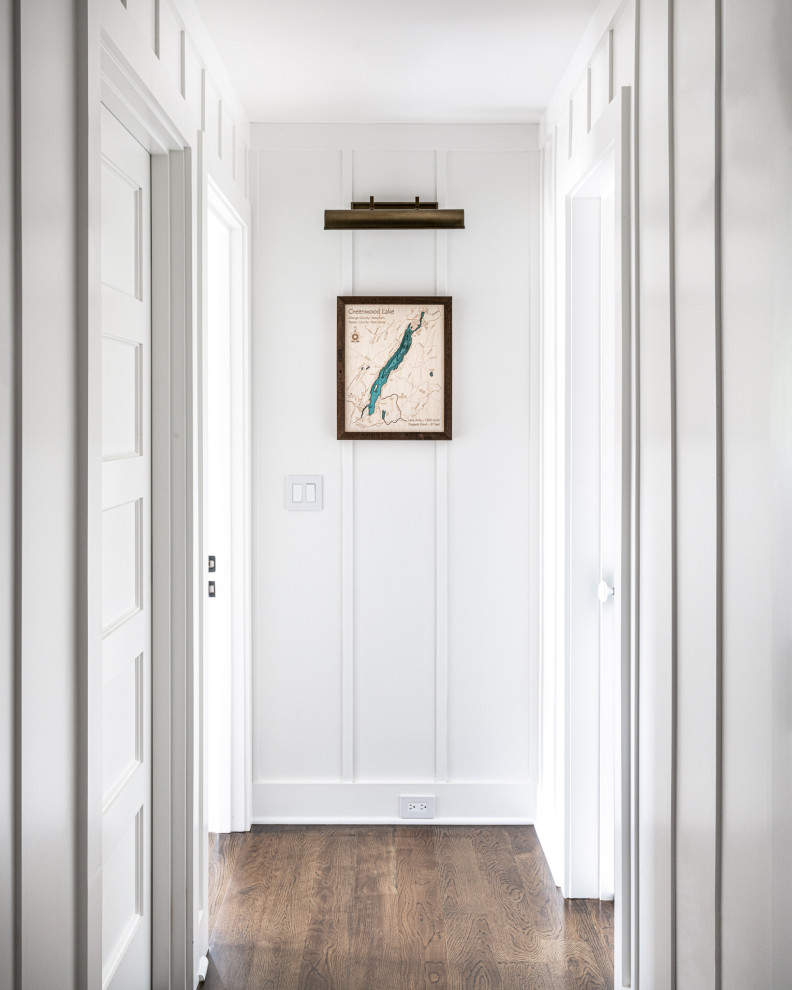 Design ideas for a transitional hallway in New York with white walls, dark hardwood floors, brown floor and decorative wall panelling.