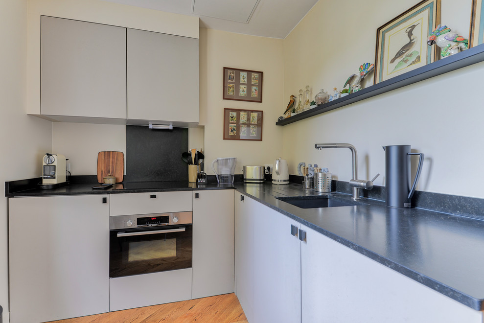 Aménagement d'une cuisine contemporaine en L de taille moyenne avec un évier encastré, un plan de travail en granite, parquet clair, un plan de travail gris, un placard à porte plane et des portes de placard grises.