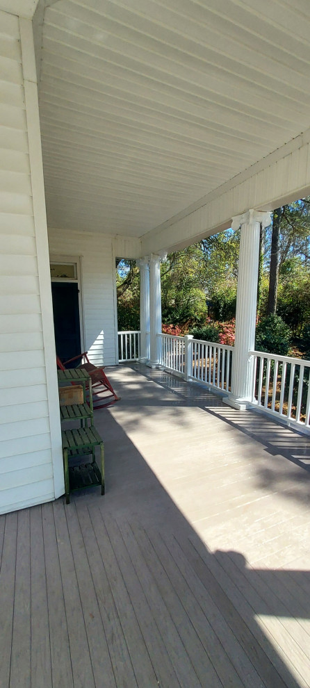 Exemple d'un grand porche d'entrée de maison avant victorien avec des colonnes, une terrasse en bois, une extension de toiture et un garde-corps en bois.