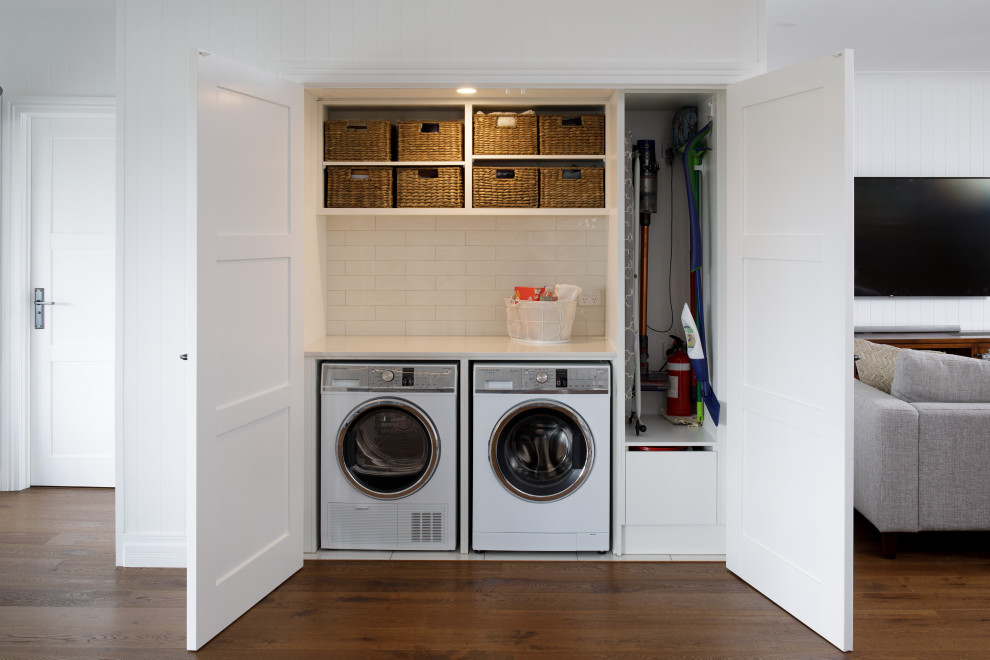 Small transitional single-wall laundry cupboard in Brisbane with quartz benchtops, white splashback, subway tile splashback, white walls, medium hardwood floors, a side-by-side washer and dryer, brown floor and white benchtop.