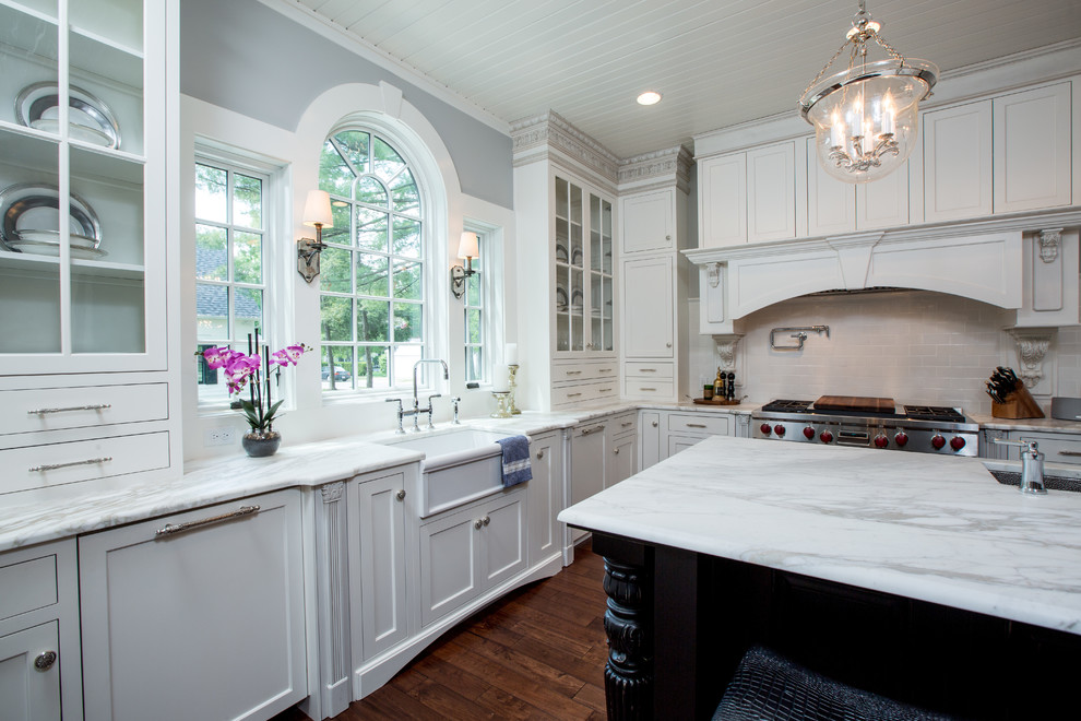 Photo of a large traditional u-shaped separate kitchen in Cincinnati with white cabinets, subway tile splashback, medium hardwood floors, with island, an undermount sink, glass-front cabinets, marble benchtops, white splashback and stainless steel appliances.