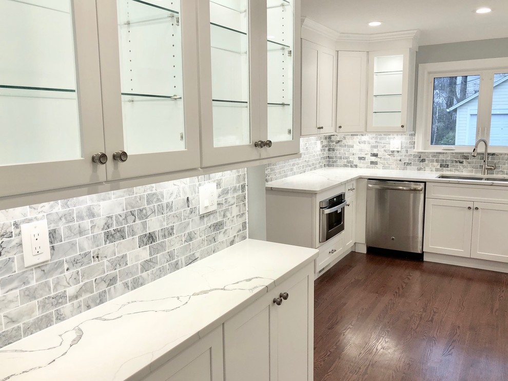 Mid-sized transitional u-shaped dark wood floor and brown floor enclosed kitchen photo with an undermount sink, shaker cabinets, white cabinets, marble countertops, gray backsplash, stone tile backsplash, stainless steel appliances, no island and white countertops