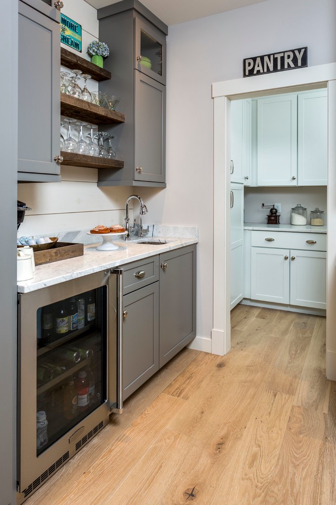 This is an example of a mid-sized arts and crafts single-wall wet bar in Portland Maine with white splashback, light hardwood floors, an undermount sink, grey cabinets, marble benchtops and shaker cabinets.