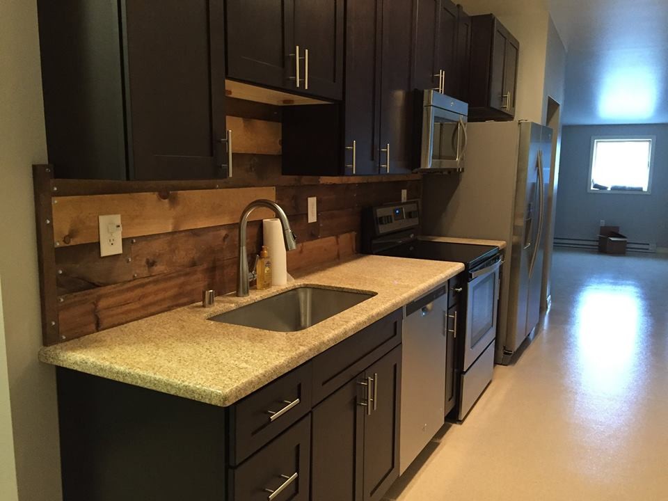 Mid-sized transitional single-wall laminate floor kitchen photo with an undermount sink, shaker cabinets, black cabinets, granite countertops, brown backsplash, wood backsplash and stainless steel appliances