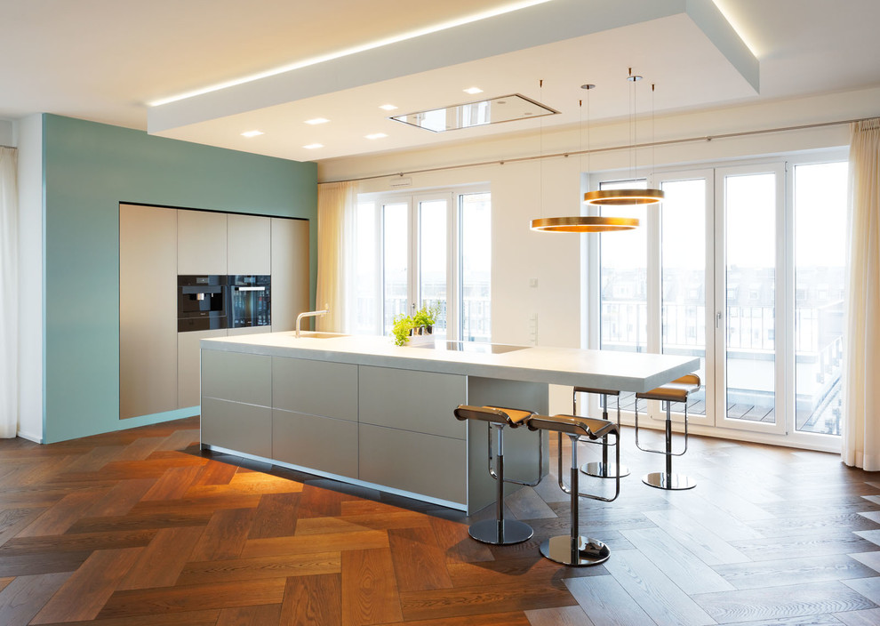 Photo of a mid-sized contemporary l-shaped kitchen in Dusseldorf with flat-panel cabinets, black appliances, dark hardwood floors, with island, stainless steel cabinets and a drop-in sink.