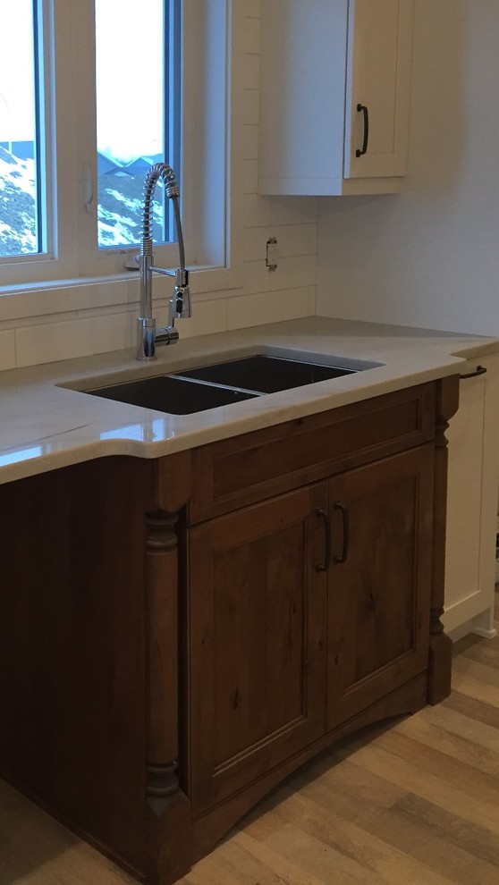 Example of a mid-sized mountain style galley medium tone wood floor and brown floor open concept kitchen design in Calgary with an undermount sink, recessed-panel cabinets, white cabinets, marble countertops, white backsplash, ceramic backsplash and a peninsula
