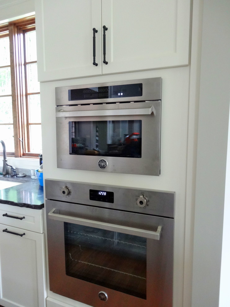 Open concept kitchen - mid-sized transitional l-shaped medium tone wood floor open concept kitchen idea in Charlotte with a farmhouse sink, shaker cabinets, white cabinets, granite countertops, beige backsplash, subway tile backsplash, stainless steel appliances and an island