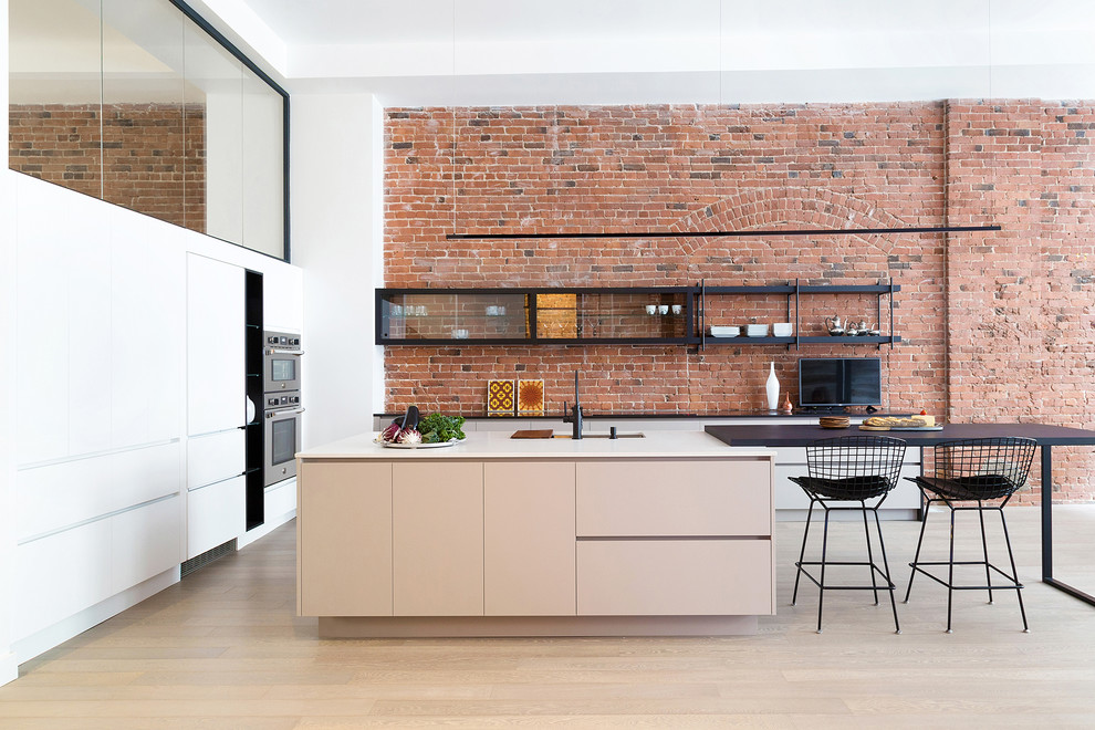 Design ideas for an industrial open plan kitchen in Montreal with white cabinets, granite benchtops, red splashback, brick splashback, stainless steel appliances, with island, black benchtop, an undermount sink, flat-panel cabinets, light hardwood floors and beige floor.
