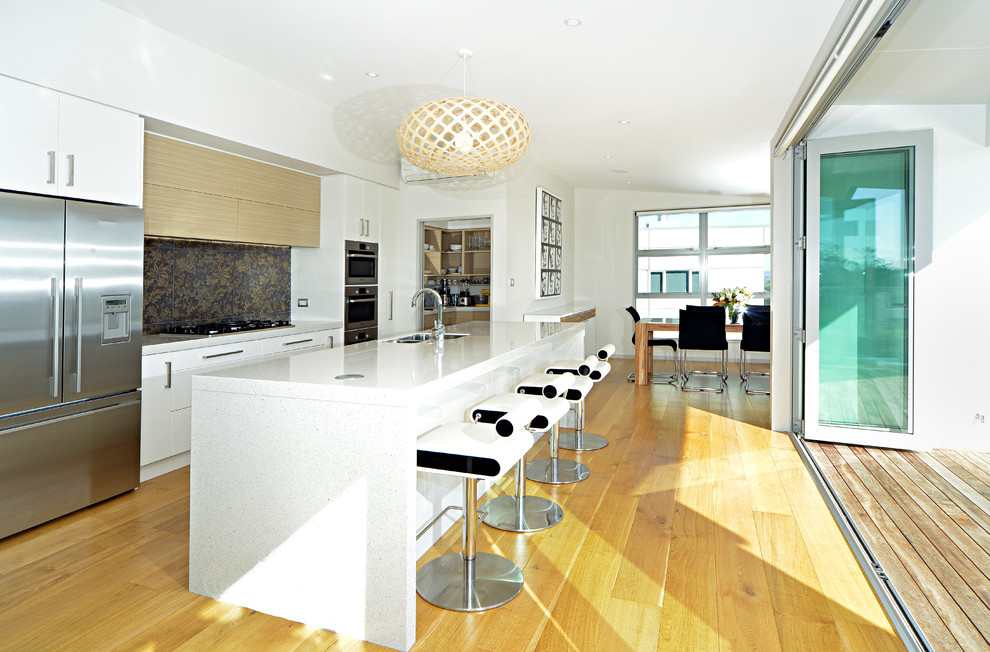 This is an example of a contemporary galley eat-in kitchen in Auckland with a double-bowl sink, flat-panel cabinets, multi-coloured splashback and stainless steel appliances.
