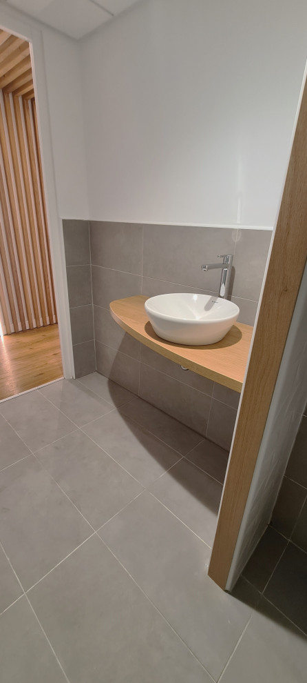 Immagine di un piccolo bagno di servizio minimalista con WC sospeso, piastrelle grigie, piastrelle in ceramica, pareti bianche, pavimento con piastrelle in ceramica, lavabo da incasso, top in legno e pavimento grigio