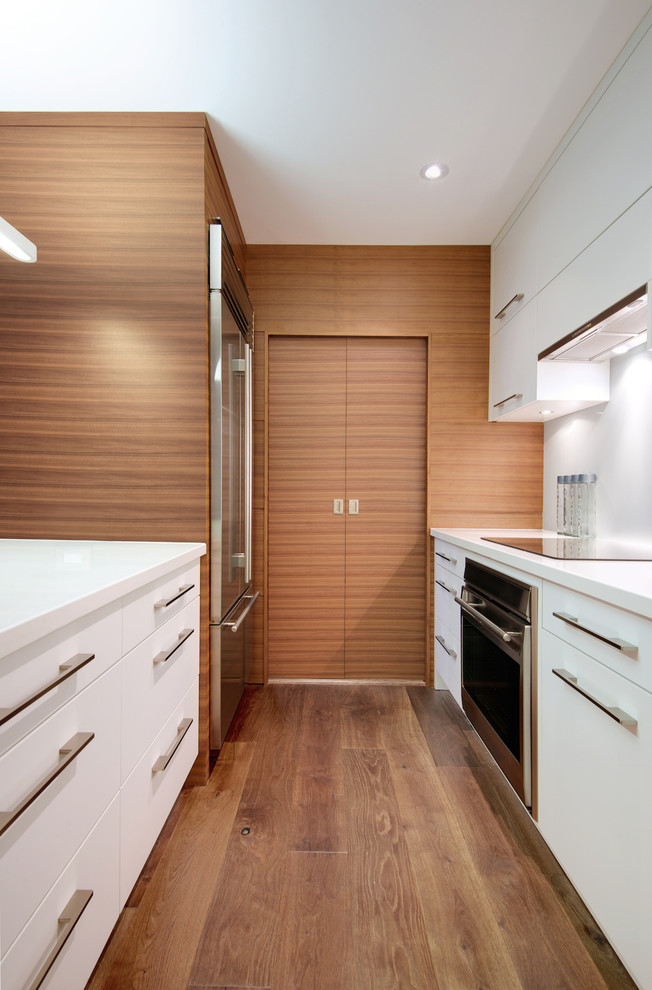 Inspiration for a small contemporary galley eat-in kitchen in Toronto with an undermount sink, flat-panel cabinets, white cabinets, quartz benchtops, white splashback, glass sheet splashback, stainless steel appliances, medium hardwood floors and with island.