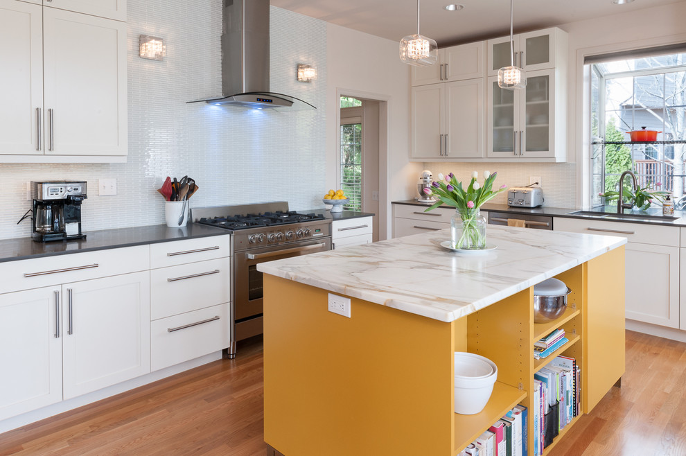 Mid-sized contemporary l-shaped open plan kitchen in Seattle with a double-bowl sink, shaker cabinets, yellow cabinets, marble benchtops, white splashback, glass tile splashback, stainless steel appliances, light hardwood floors and with island.