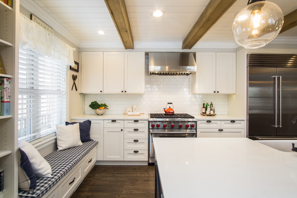 This is an example of a country kitchen in Chicago with a farmhouse sink, shaker cabinets, white cabinets, quartzite benchtops, white splashback, ceramic splashback, stainless steel appliances, dark hardwood floors, with island, brown floor and white benchtop.