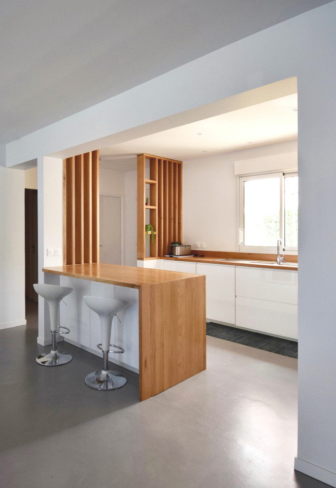 Photo of a mid-sized contemporary single-wall open plan kitchen in Montpellier with white cabinets, wood benchtops, grey floor, a single-bowl sink, open cabinets, brown splashback, timber splashback, no island and brown benchtop.