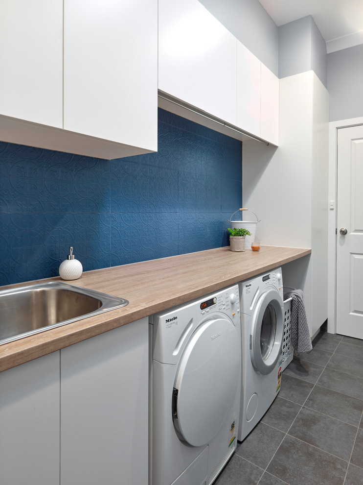 Small contemporary single-wall dedicated laundry room in Other with a drop-in sink, flat-panel cabinets, white cabinets, laminate benchtops, blue walls, porcelain floors, a side-by-side washer and dryer, grey floor and orange benchtop.