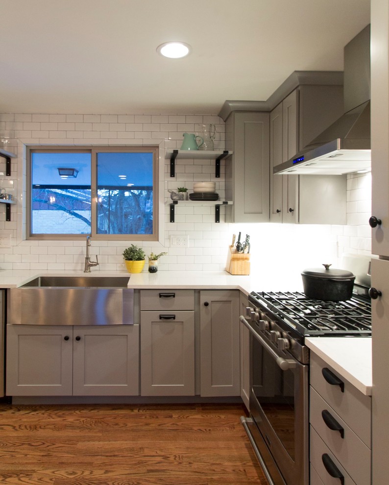Eat-in kitchen - mid-sized transitional l-shaped medium tone wood floor eat-in kitchen idea in Denver with a farmhouse sink, shaker cabinets, gray cabinets, quartz countertops, white backsplash, ceramic backsplash, stainless steel appliances and an island