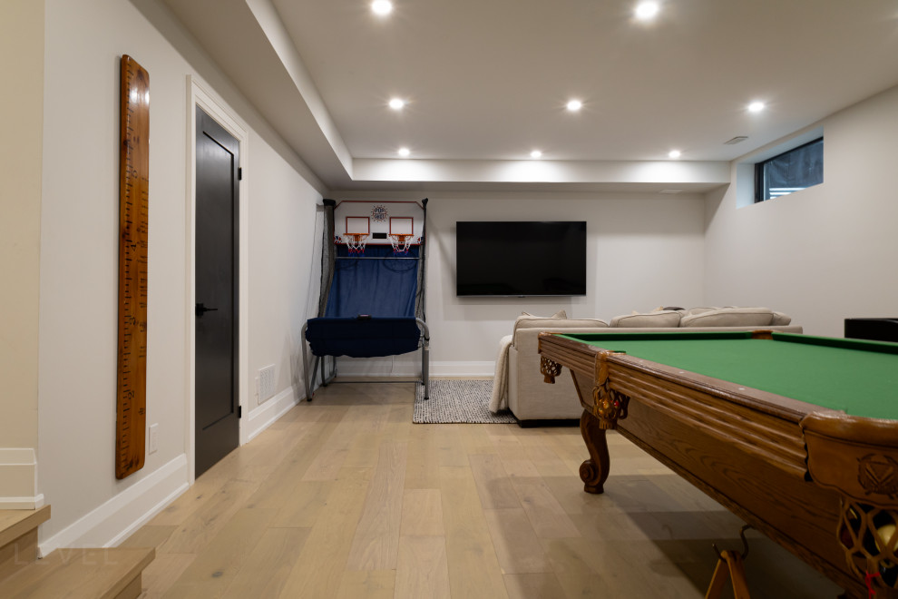 Стильный дизайн: большая открытая комната для игр в современном стиле с белыми стенами, светлым паркетным полом, телевизором на стене и коричневым полом - последний тренд