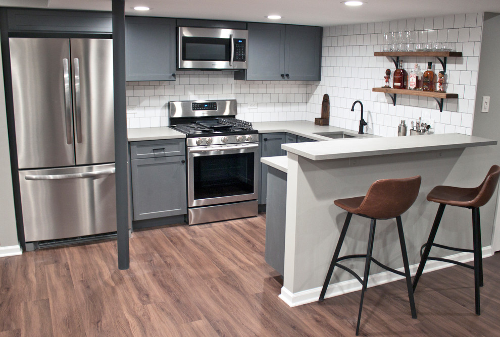 Mid-sized transitional u-shaped vinyl floor open concept kitchen photo in Chicago with an undermount sink, shaker cabinets, gray cabinets, quartz countertops, white backsplash, ceramic backsplash, stainless steel appliances, a peninsula and gray countertops