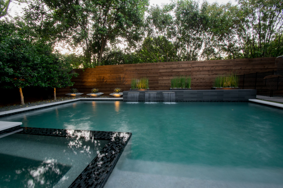 This is an example of a small modern backyard custom-shaped pool in Dallas with with privacy feature and natural stone pavers.