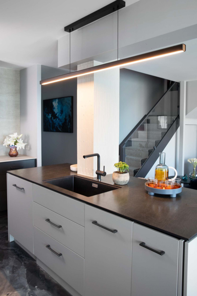 Inspiration for a small modern l-shaped gray floor open concept kitchen remodel in Brisbane with an undermount sink, flat-panel cabinets, gray cabinets, solid surface countertops, white backsplash, stone slab backsplash, black appliances, an island and black countertops