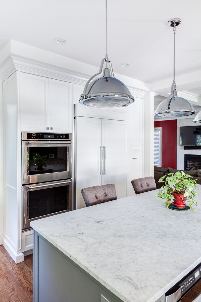 Mid-sized transitional u-shaped open plan kitchen in New York with a farmhouse sink, shaker cabinets, white cabinets, quartz benchtops, grey splashback, glass tile splashback, panelled appliances, light hardwood floors, with island and brown floor.