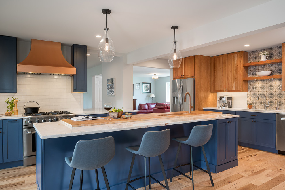 Photo of a large transitional l-shaped eat-in kitchen in Burlington with an undermount sink, shaker cabinets, blue cabinets, quartzite benchtops, white splashback, porcelain splashback, stainless steel appliances, light hardwood floors, with island and white benchtop.