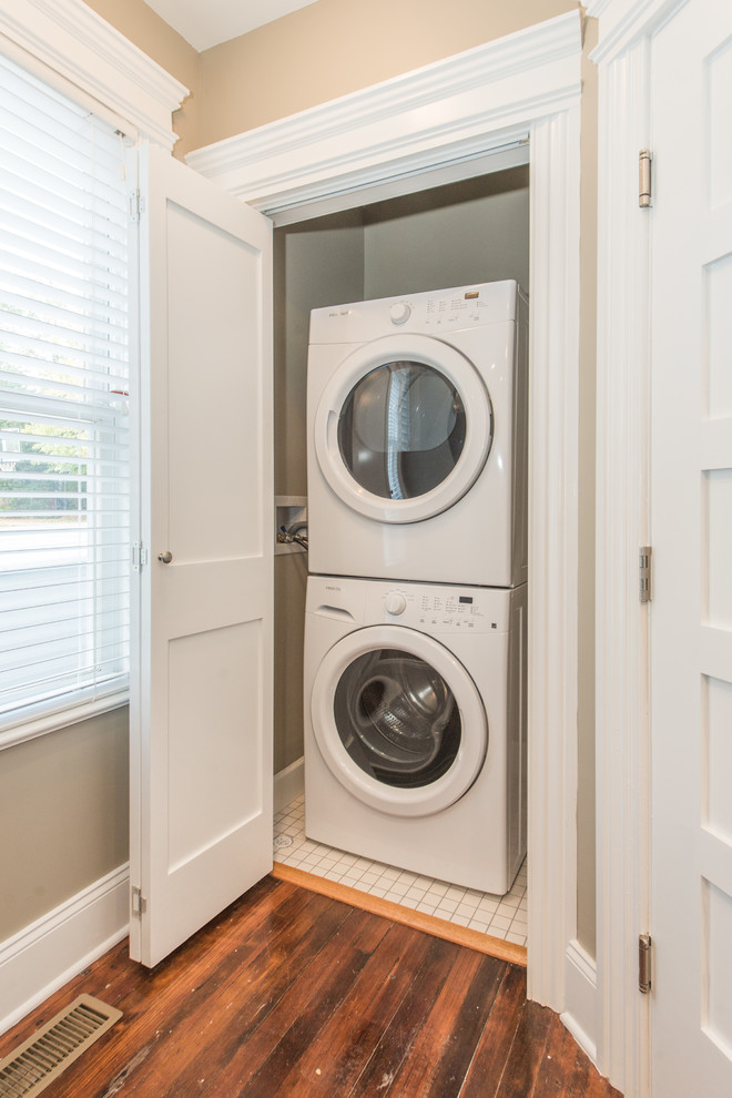 Photo of a small transitional laundry cupboard in New York with beige walls, dark hardwood floors, a stacked washer and dryer and brown floor.