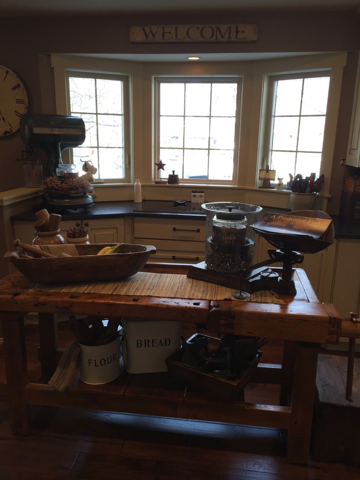Example of a mid-sized mountain style l-shaped dark wood floor enclosed kitchen design in Minneapolis with a farmhouse sink, raised-panel cabinets, distressed cabinets, granite countertops, black backsplash, stainless steel appliances and an island