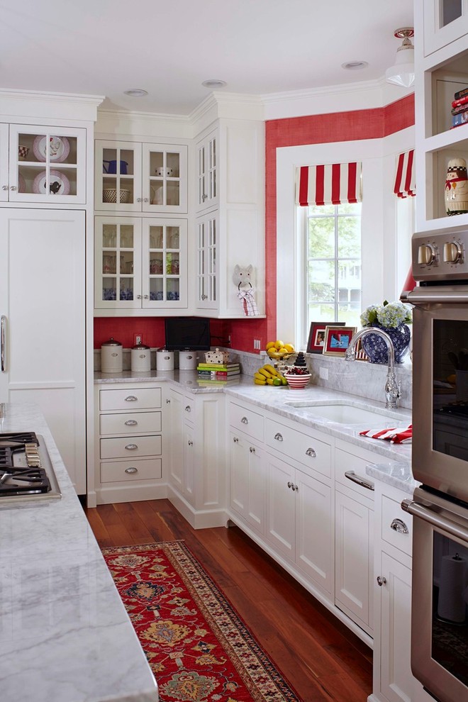 This is an example of a mid-sized traditional single-wall open plan kitchen in Portland Maine with an undermount sink, white cabinets, white splashback, shaker cabinets, marble benchtops, stainless steel appliances, medium hardwood floors, brown floor, white benchtop and with island.
