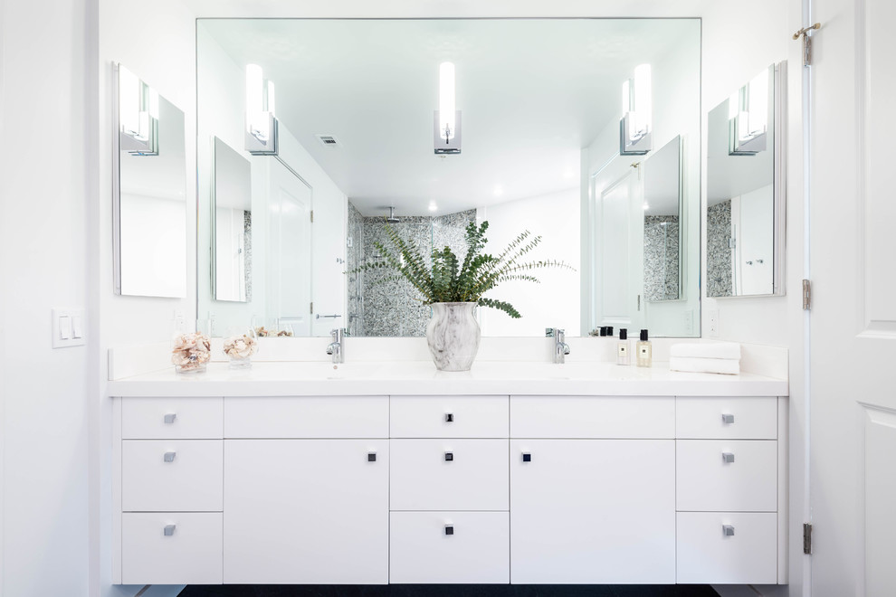 Photo of a mid-sized contemporary master bathroom in DC Metro with flat-panel cabinets, white cabinets, a corner tub, an alcove shower, a two-piece toilet, multi-coloured tile, mosaic tile, white walls, marble floors, an undermount sink, solid surface benchtops, grey floor, a hinged shower door and white benchtops.