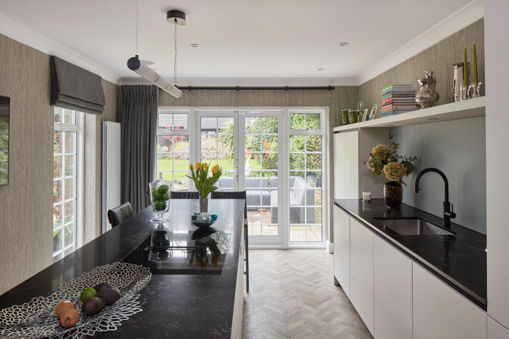 Design ideas for a mid-sized modern single-wall separate kitchen in London with an undermount sink, flat-panel cabinets, white cabinets, quartz benchtops, grey splashback, glass sheet splashback, black appliances, medium hardwood floors, with island, brown floor and black benchtop.
