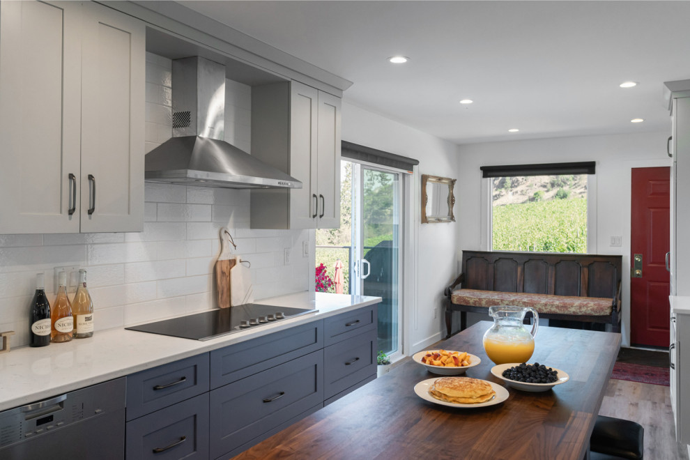 Eat-in kitchen - mid-sized transitional u-shaped medium tone wood floor and brown floor eat-in kitchen idea with recessed-panel cabinets, gray cabinets, quartz countertops, white backsplash, ceramic backsplash, stainless steel appliances, an island and white countertops