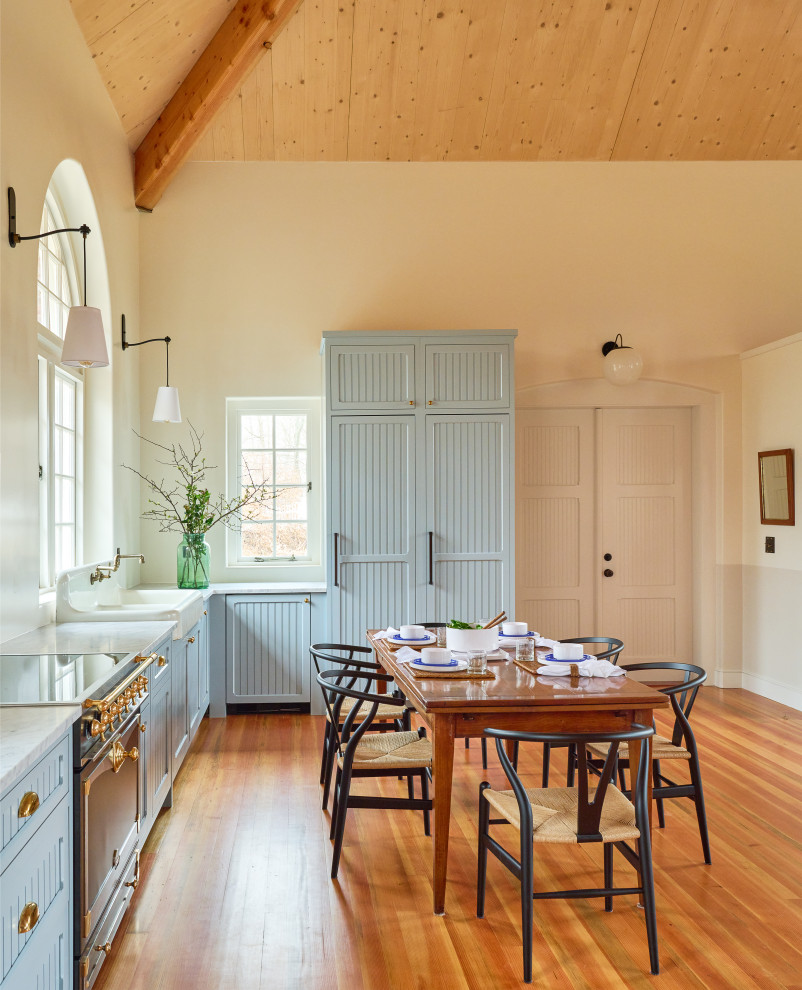Photo of a traditional l-shaped open plan kitchen in New York with a farmhouse sink, recessed-panel cabinets, blue cabinets, marble benchtops, panelled appliances, light hardwood floors, white benchtop and vaulted.