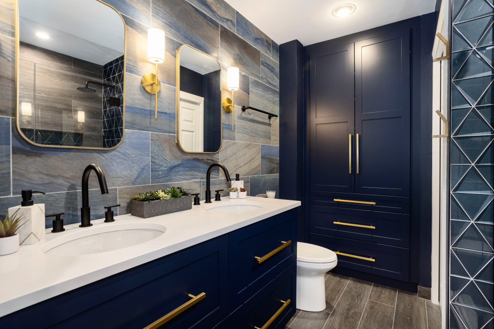 Design ideas for a medium sized modern ensuite bathroom in Chicago with blue cabinets, double sinks, blue walls, wood-effect flooring, shaker cabinets, an alcove shower, a two-piece toilet, grey tiles, wood-effect tiles, a submerged sink, grey floors, a wall niche, a built in vanity unit and white worktops.