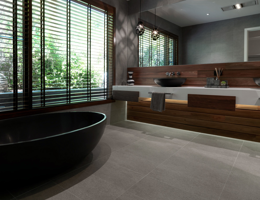 Photo of a large contemporary master bathroom in Melbourne with a vessel sink, medium wood cabinets, granite benchtops, a freestanding tub, gray tile, cement tile, grey walls and concrete floors.