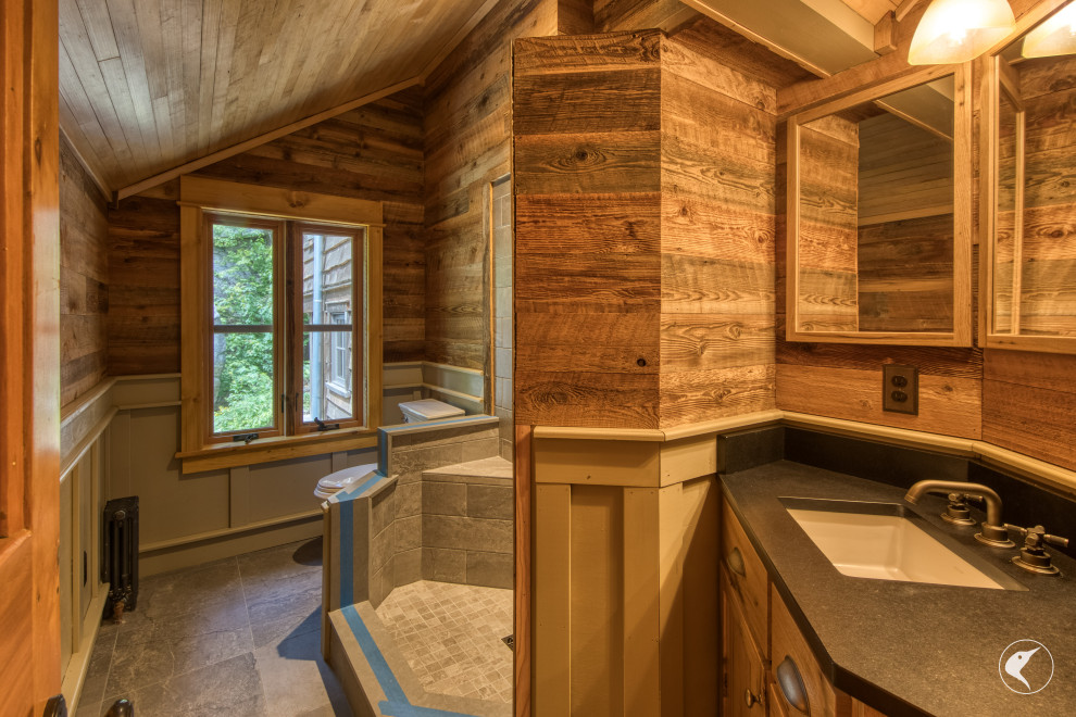 Mountain style porcelain tile, single-sink, wood ceiling and wainscoting shower bench photo with shaker cabinets, an undermount sink, granite countertops, a hinged shower door, black countertops and a built-in vanity