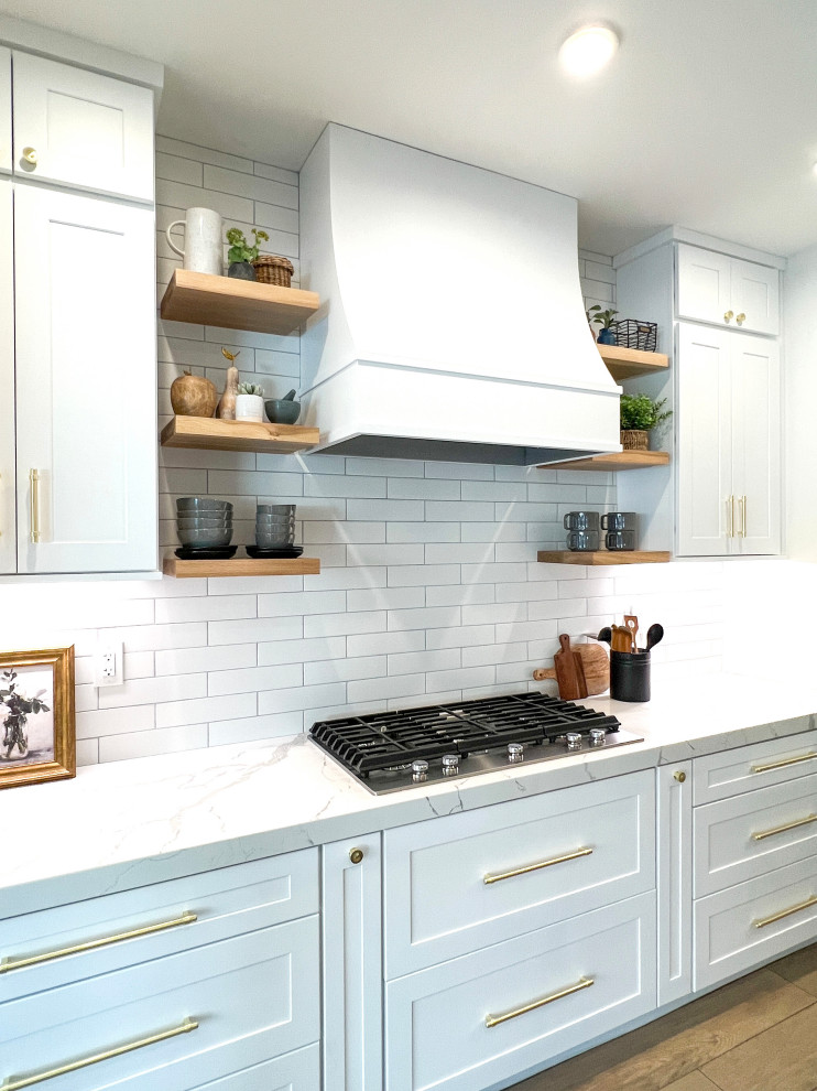 Design ideas for a mid-sized country kitchen in Orange County with a farmhouse sink, shaker cabinets, white cabinets, quartz benchtops, white splashback, ceramic splashback, stainless steel appliances, porcelain floors, with island and white benchtop.