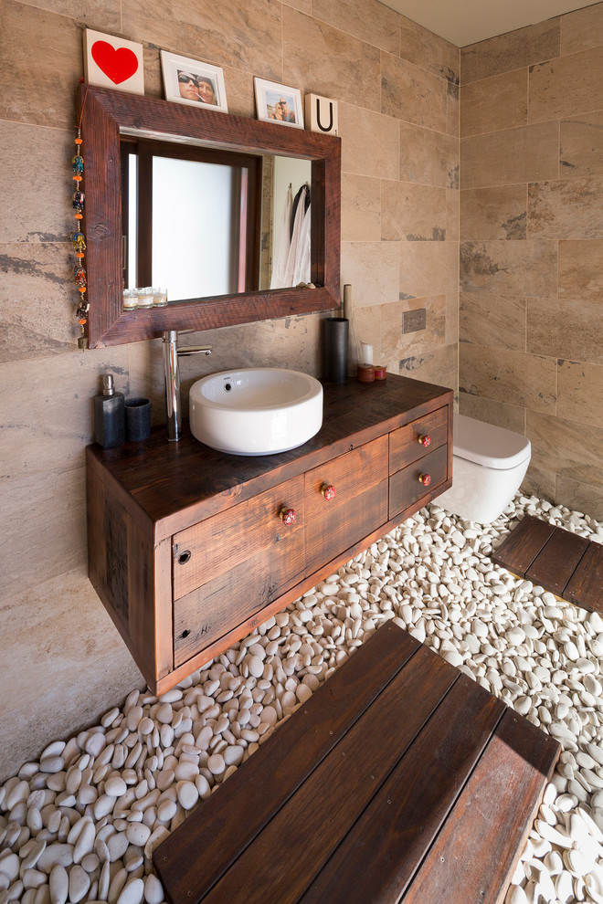 This is an example of a mid-sized asian master bathroom in Sydney with a vessel sink, a wall-mount toilet, flat-panel cabinets, dark wood cabinets, beige tile, stone slab, wood benchtops and brown benchtops.