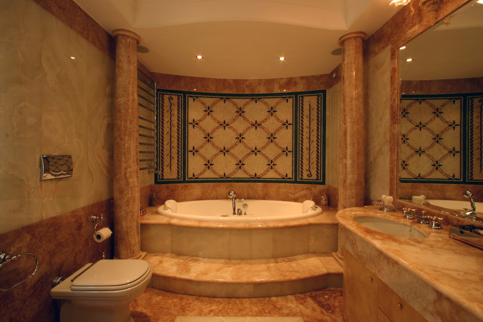 This is an example of an expansive traditional master bathroom in Rome with a drop-in sink, furniture-like cabinets, medium wood cabinets, marble benchtops, a drop-in tub, an alcove shower, a wall-mount toilet, beige tile, beige walls and marble floors.