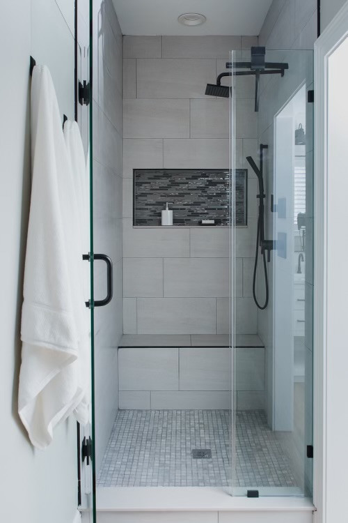 This is an example of a medium sized farmhouse ensuite bathroom in Raleigh with white cabinets, a freestanding bath, an alcove shower, a two-piece toilet, grey tiles, ceramic tiles, grey walls, laminate floors, a built-in sink, brown floors, a hinged door, white worktops, a wall niche, double sinks, a freestanding vanity unit and tongue and groove walls.