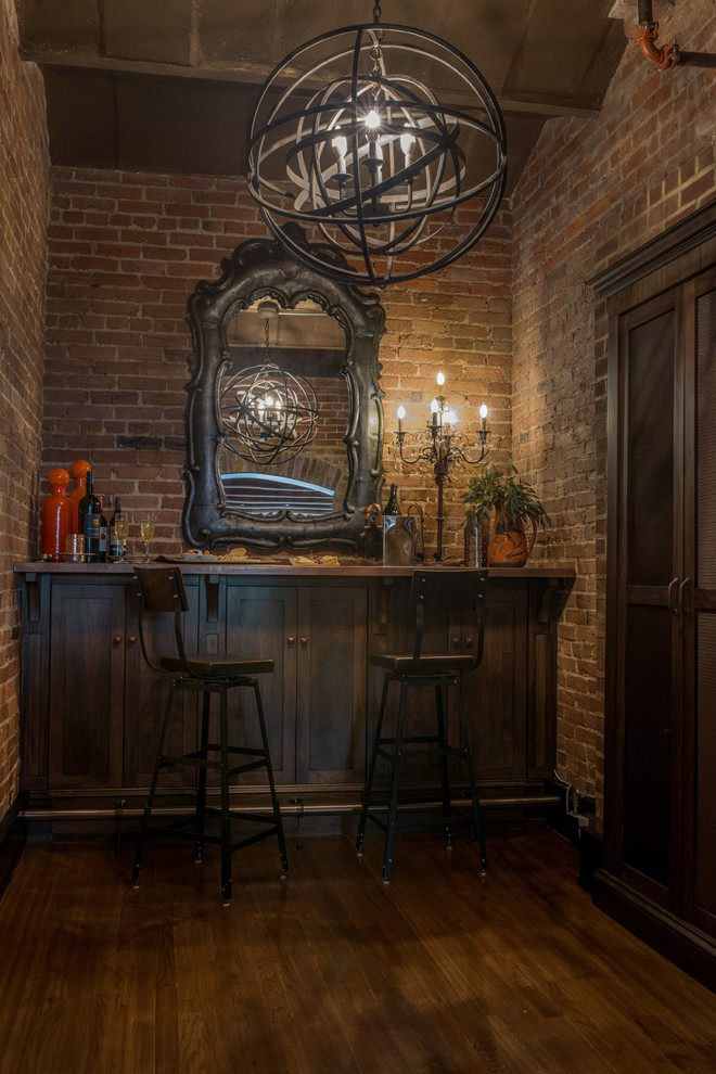 This is an example of an industrial seated home bar in Philadelphia with wood benchtops, brown floor, no sink, shaker cabinets, dark wood cabinets, red splashback, brick splashback and dark hardwood floors.