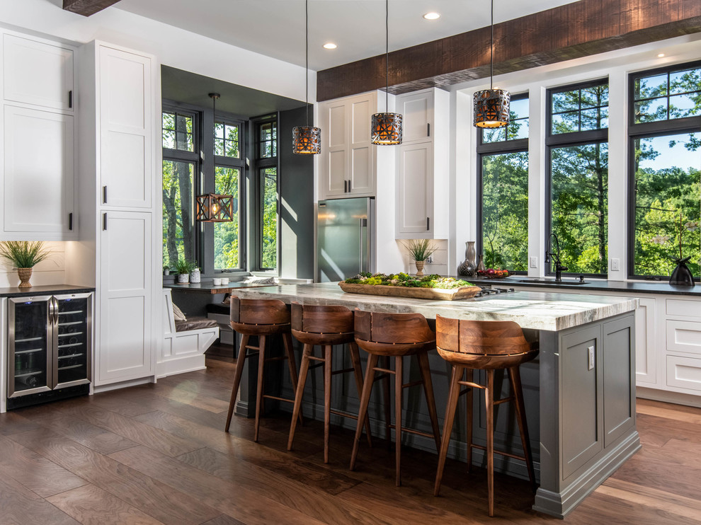 This is an example of a large country l-shaped eat-in kitchen in Other with shaker cabinets, white cabinets, stainless steel appliances, dark hardwood floors, with island, brown floor, black benchtop, an undermount sink, granite benchtops, white splashback and window splashback.